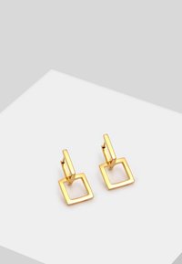Boucles d'oreilles en or avec un design carré. Texture lisse, forme minimaliste, dotées d'une attache à levier pour un maintien sécurisé.