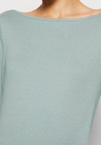 Jasnoniebieska bluzka z długim rękawem, wykonana z miękkiej, elastycznej bawełny. Posiada szeroki dekolt oraz gładką fakturę z dopasowanym krojem.