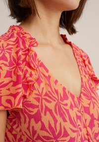 Floral patterned dress in orange and pink with ruffled neckline. Features a V-neck and textured fabric for added detail.