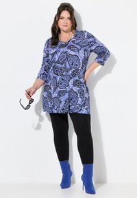 Tunika s modrým paisley vzorem a tříčtvrtečními rukávy, zkombinovaná s černými legínami a modrými kotníkovými botami. Hladký materiál s volným střihem.