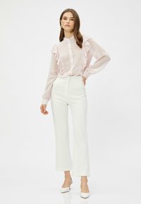 Lyserød bluse med rynker og lange ærmer, knappelukning. Et par hvide skræddersyede bukser med cropped, flagrende ben og lyse hæle.