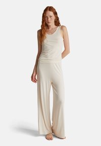 Jasno-beżowy top na ramiączkach z szerokimi paskami, w połączeniu z dopasowanymi, luźnymi spodniami palazzo z miękkiego materiału. Szczegóły szwów w pasie.