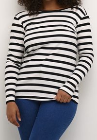 Haut à manches longues à rayures noires et blanches avec une texture côtelée, un col rond et des manches ajustées, associé à un jean en denim bleu.