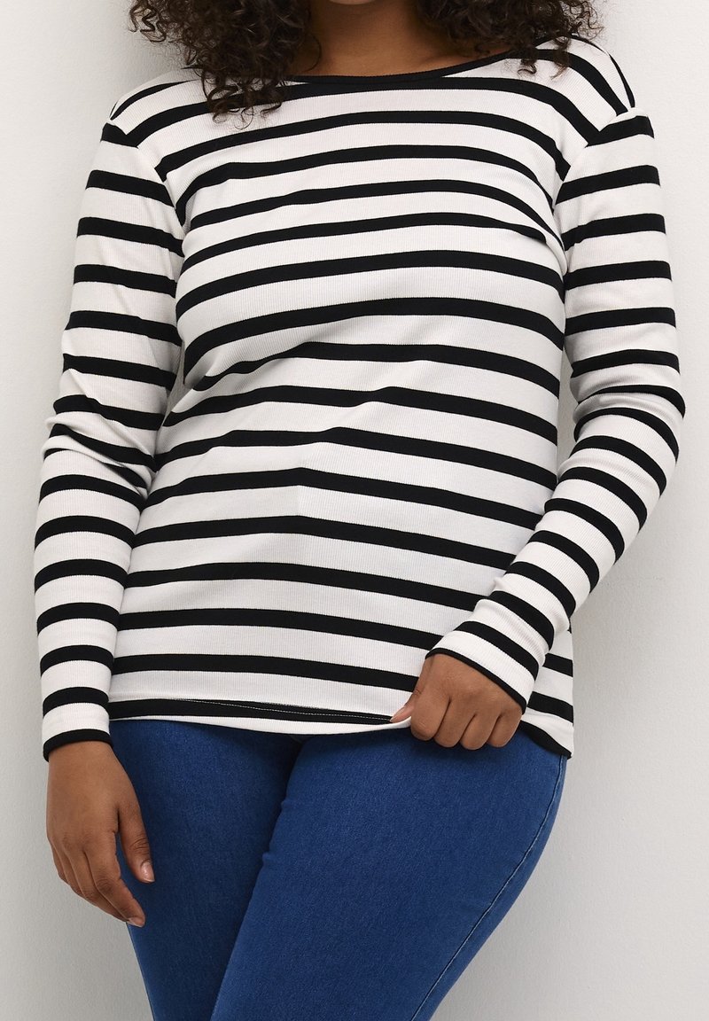 Haut à manches longues à rayures noires et blanches avec une texture côtelée, un col rond et des manches ajustées, associé à un jean en denim bleu.