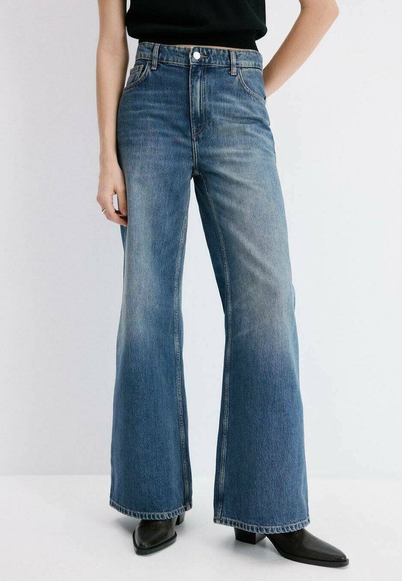 Femme portant un jean bleu taille haute à jambes larges avec un léger délavage, associé à des bottines noires à bout pointu et un haut noir.