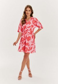 Růžové šaty s akvarelovým vzorem v červených odstínech. Mají výstřih do V, krátké rukávy a úzký pas s látkovým páskem.