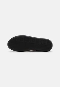 Semelle de chaussure noire avec un motif de bande de roulement ondulé et le nom de la marque embossé inversé "HILFIGER" visible en bas.