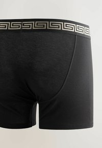 Schwarze Boxershorts mit einem Markenbund, der ein geometrisches Muster aufweist, auf einem schlichten hellen Hintergrund präsentiert.