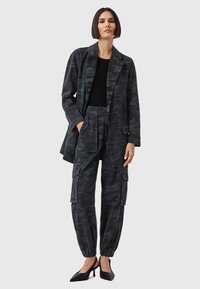 Set di giacca e pantaloni con motivo camouflage nero. Giacca: lunga, vestibilità ampia, tasche. Pantaloni: con fondo ristretto, tasche cargo. Entrambi in tessuto testurizzato.