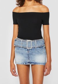 Žena v černém topu bez ramínek a světle modré mini sukni z acid-wash denimu s širokým opaskem a velkou obdélníkovou sponou.