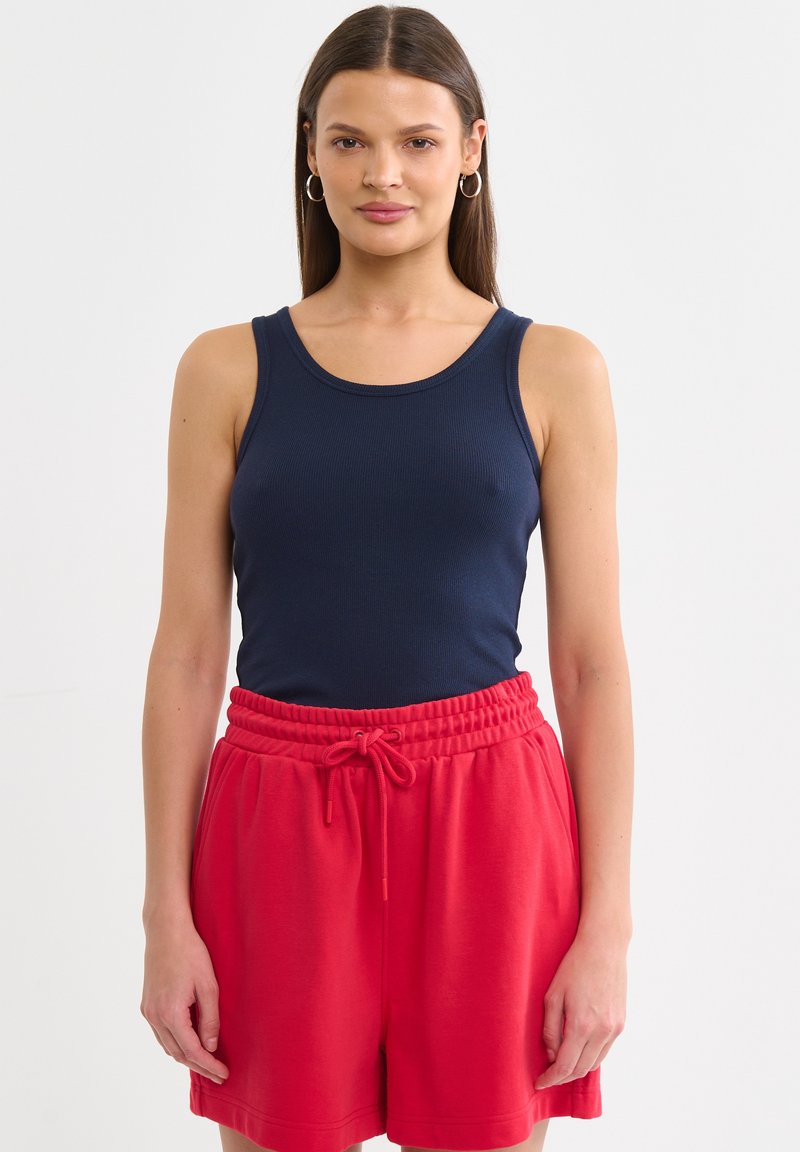 Námorně modrý žebrovaný top bez rukávů spárovaný s červenými šortkami na stažení. Outfit se vyznačuje přiléhavým střihem a měkkou texturou.
