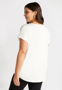 Camiseta blanca de manga corta con dobladillo redondeado, textura suave y corte relajado, vista desde la parte posterior. Sin patrones ni adornos visibles.
