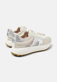 Beige sneakers med ovandel i mesh, silverdetaljer och en tjock vit gummisula. Har snörning och en logotyp på hälen.