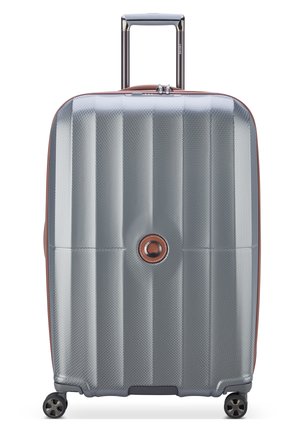 Valigia rigida di colore argento con superficie testurizzata, dettagli marroni a contrasto, manico telescopico e quattro ruote nere.