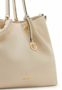 Borsa a tracolla in pelle beige con texture, doppie tracolle, finiture dorate e un ciondolo rotondo dorato appeso a una delle tracolle.