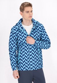 Modra dežna jakna s chevron vzorcem, ki vključuje kapuco, zadrgo spredaj in elastične manšete, izdelana iz lahkotnega materiala.
