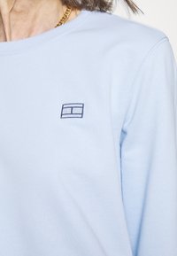 Camiseta de manga larga azul claro, hecha de algodón suave, con un pequeño logotipo bordado en color marino en el lado izquierdo del pecho.