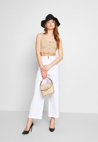 Top cropped bege com botões, calças brancas de perna larga, sapatos de salto alto pretos e uma bolsa texturizada bege. Chapéu preto de aba larga.