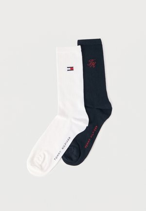 Pari ribbilaistaa sukkia, toinen valkoinen, jossa Tommy Hilfiger -lipputunnus ja musta teksti, toinen musta, jossa punainen kirjailtu "TH" ja vastaava teksti jalassa.