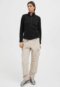 Pull en polaire noir avec col haut et demi-zip, associé à un pantalon cargo beige avec de multiples poches et une coupe décontractée.