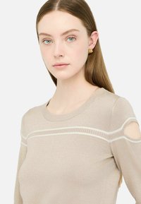 Beige Strickpullover mit Rundhalsausschnitt, ausgeschnittenen Schulterdetails und einem strukturierten Muster mit einem kontrastierenden Streifen über der Brust.
