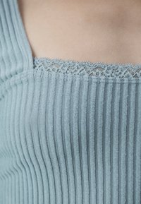 Ljust blå ribbad tygtröja med smala vertikala ränder och delikat spetsdetalj längs halslinningen. Slät struktur, figurnära design.