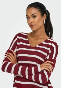 Pull en tricot rayé bordeaux et blanc avec un décolleté en V et des manches longues, présentant une coupe décontractée et une texture douce.