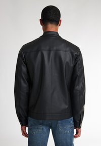 Zwarte leren jacket met een gladde textuur, voorzien van een kraag en knoopmanchetten, getoond vanaf de achterkant tegen een neutrale achtergrond.