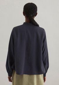 Blusa blu scuro con maniche lunghe e vaporose e colletto alla cinese, realizzata in un tessuto liscio. La parte posteriore è leggermente curvata con una vestibilità rilassata.