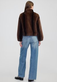 Braune Kunstfelljacke mit hohem Kragen, lockerer Passform und schwarzen vertikalen Streifen, kombiniert mit hellblauen weiten Jeans und schwarzen Schuhen.