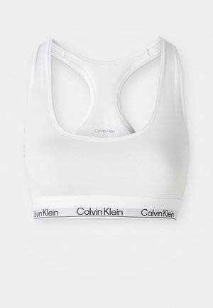 Bijeli pamukasti bralette s izrezom u obliku žlice i dizajnom s racerback leđima. Ima crnu elastičnu traku s brendom na dnu. Glatka tekstura.