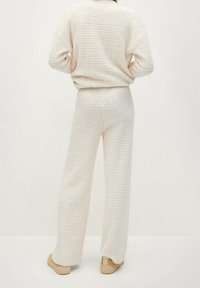 Witte gebreide trui met textuur en wijd uitlopende broek, beide met een losse pasvorm. De stof lijkt zacht te zijn, met een subtiel patroon overal.