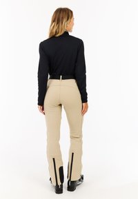 Beige skibukser med sorte detaljer, høj talje og sidelommer. Langærmet sort top, glat stof, tætsiddende design, minimal detaljering.