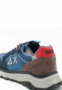 Scarpa sportiva blu realizzata con un mix di materiali tessili e scamosciati. Presenta accenti grigi, un tallone rosso con '1968' e una suola decorata per una migliore aderenza.