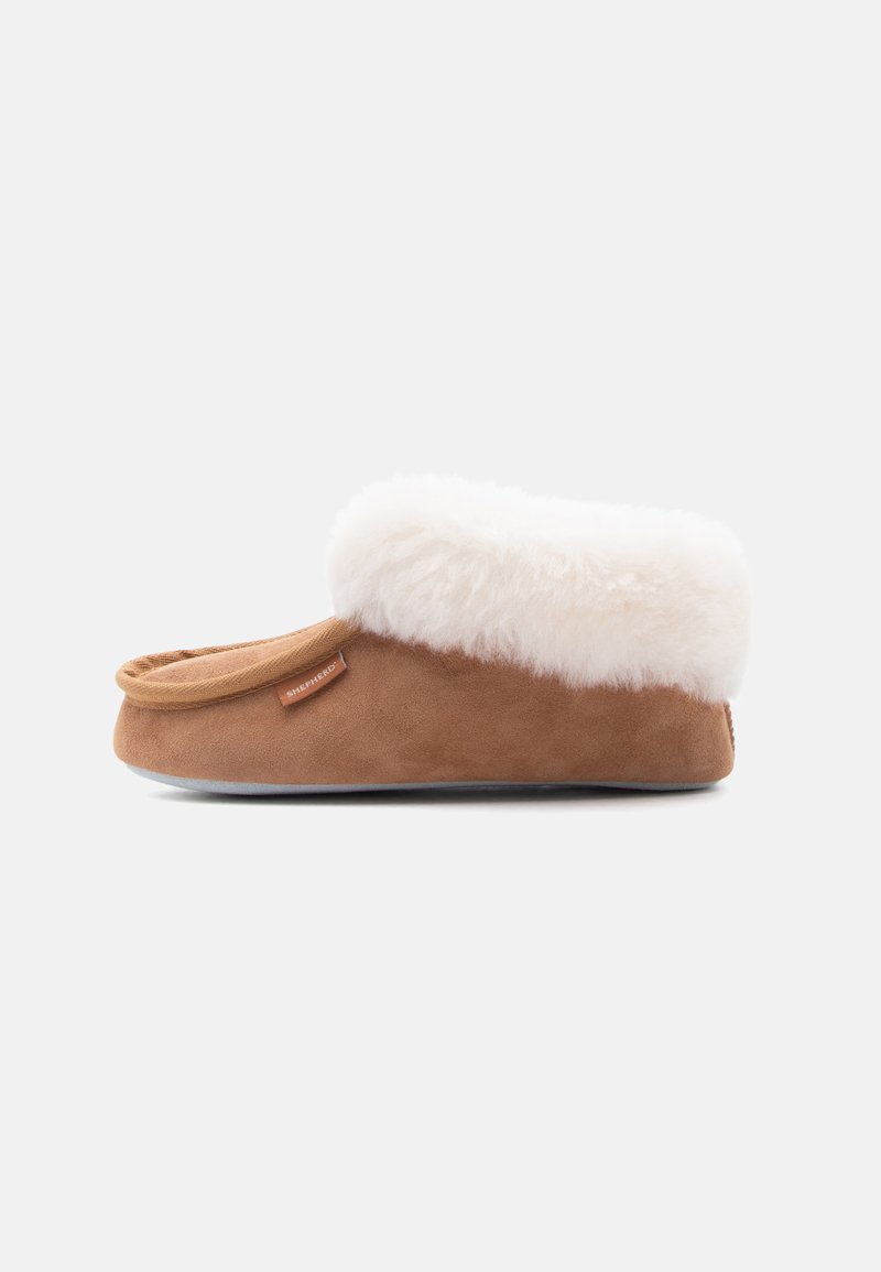 Chausson en daim marron avec doublure blanche épaisse et moelleuse et petit talon, vu de côté sur un fond uni.