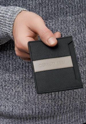 Mano sosteniendo una cartera Cerruti 1881 de cuero negro con una franja beige, sobre un fondo de suéter tejido gris.