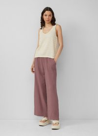 Débardeur crème sans manches avec un motif texturé, associé à un pantalon large mauve clair et ample ainsi qu'à des sandales à plateforme.