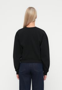 Hanorac negru cu guler rotund, umeri căzuți și tiv din tricot. Purtați-l cu blugi negri evazați, care au buzunare la spate.