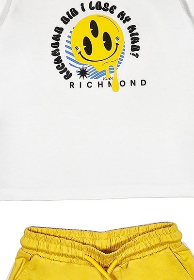 T-shirt bianca in cotone con una grafica di un sorriso giallo con dettagli neri e strisce blu, abbinata a pantaloni corti gialli con coulisse.