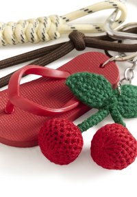 Porte-clés avec une petite tong rouge et des cerises crochetées avec des feuilles vertes, attachés à des anneaux métalliques et des cordons.