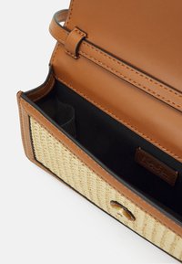Hnědá kabelka z umělé kůže s pleteným detailem ze slámy. Interiér je černá látka, vybavená přehazovací klopou a zlatým zapínáním na knoflík.