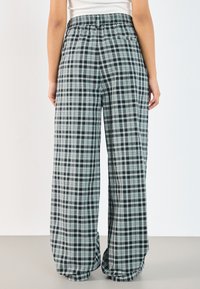 Weite Hosen mit einem schwarz-mintgrünen Karomuster, einem elastischen Bund und einem weichen, leichten Stoff.
