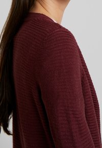Bordeaux stickad cardigan med ribbad textur, med en avslappnad passform och öppen frontdesign som framhäver dess mjuka och varma material.