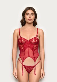 Bodysuit en dentelle rouge et maille transparente avec bretelles réglables, motifs floraux et design ajusté mettant en valeur la taille et les hanches.