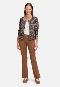 Veste zippée à motif léopard avec des manches trois-quarts, accompagnée de pantalons évasés en daim brown et de baskets beiges avec des lacets crème.