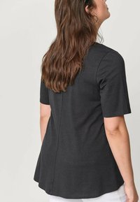 Czarny t-shirt z krótkim rękawem o zaokrąglonym dole, wykonany z miękkiego materiału, z prostym wzorem i subtelnym szwem biegnącym wzdłuż pleców.
