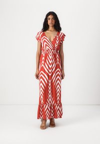 Maxime dress in orange with white chevron pattern, featuring short ruffled sleeves and an elastic waist. Flared hem with ruffle detail.