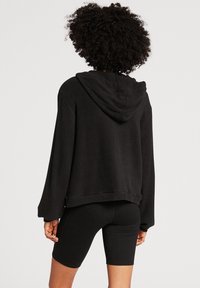 Zwarte cropped hoodie met een capuchon, lange mouwen en een zachte textuur. Gecombineerd met zwarte fietsbroeken, met een gladde stoffen afwerking.