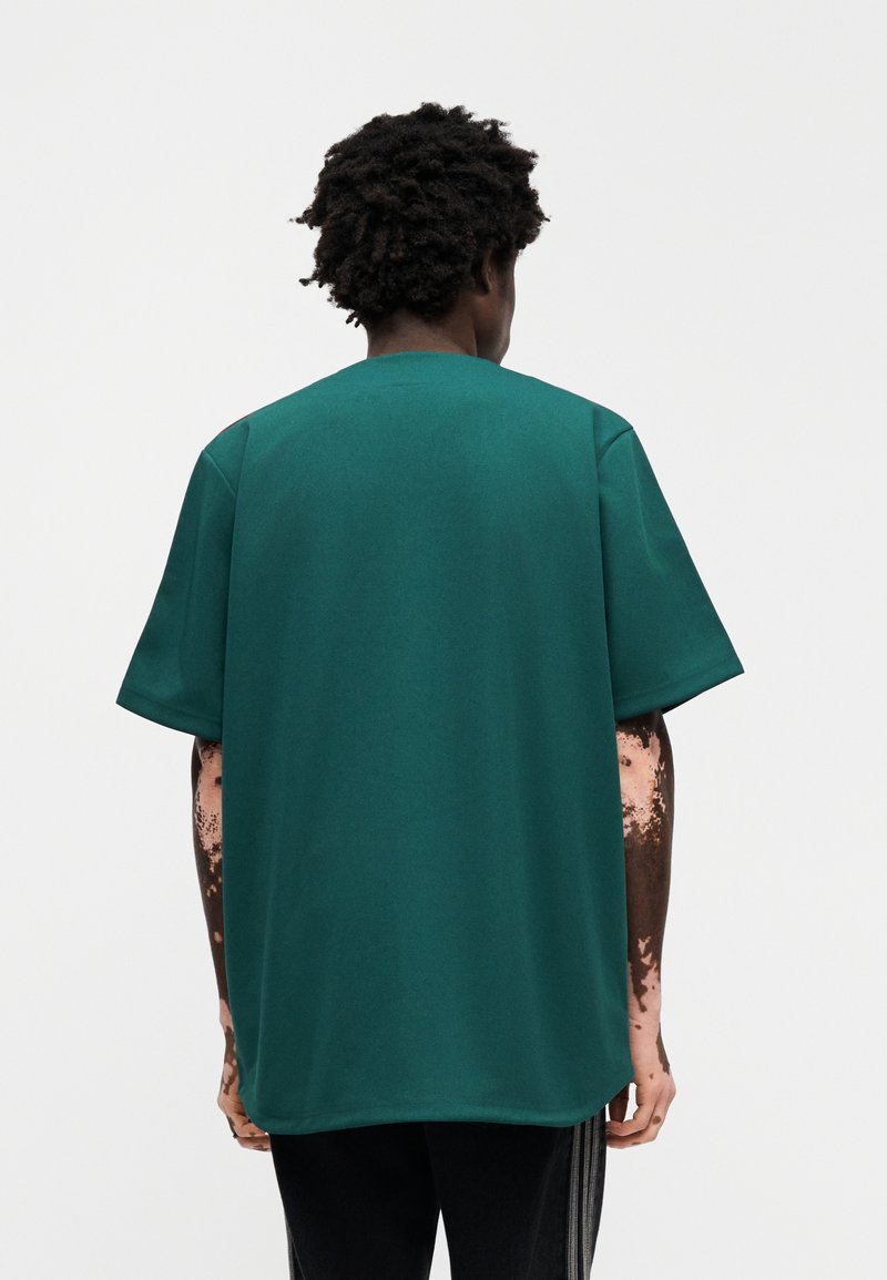 T-shirt vert à manches courtes en coton, avec une coupe décontractée et un col rond, texture lisse sans motifs visibles.