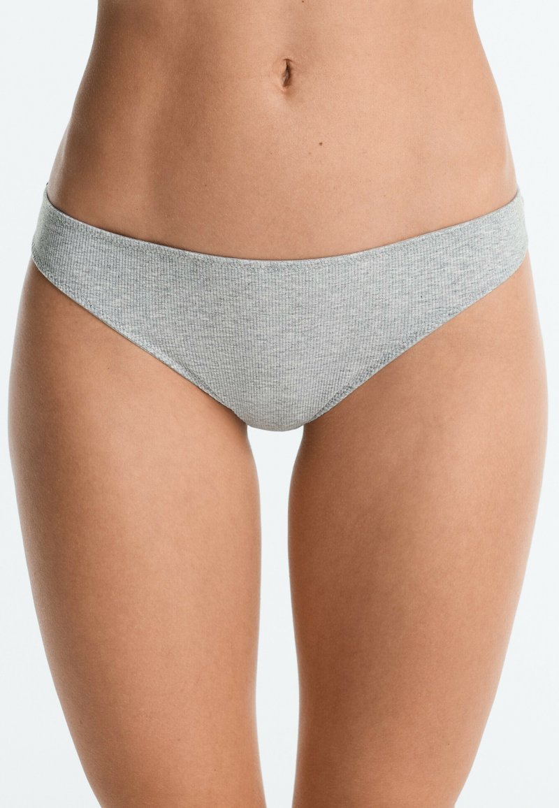 Personne portant des sous-vêtements côtelés gris clair, montrée du milieu du torse au haut des cuisses sur un fond clair et uni.